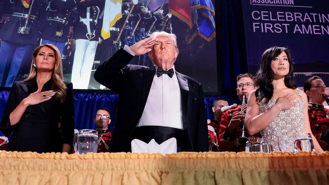 Melania Trump and Weijia Jiang stand with hands over their hearts, flanking a saluting Donald Trump at a banquet table