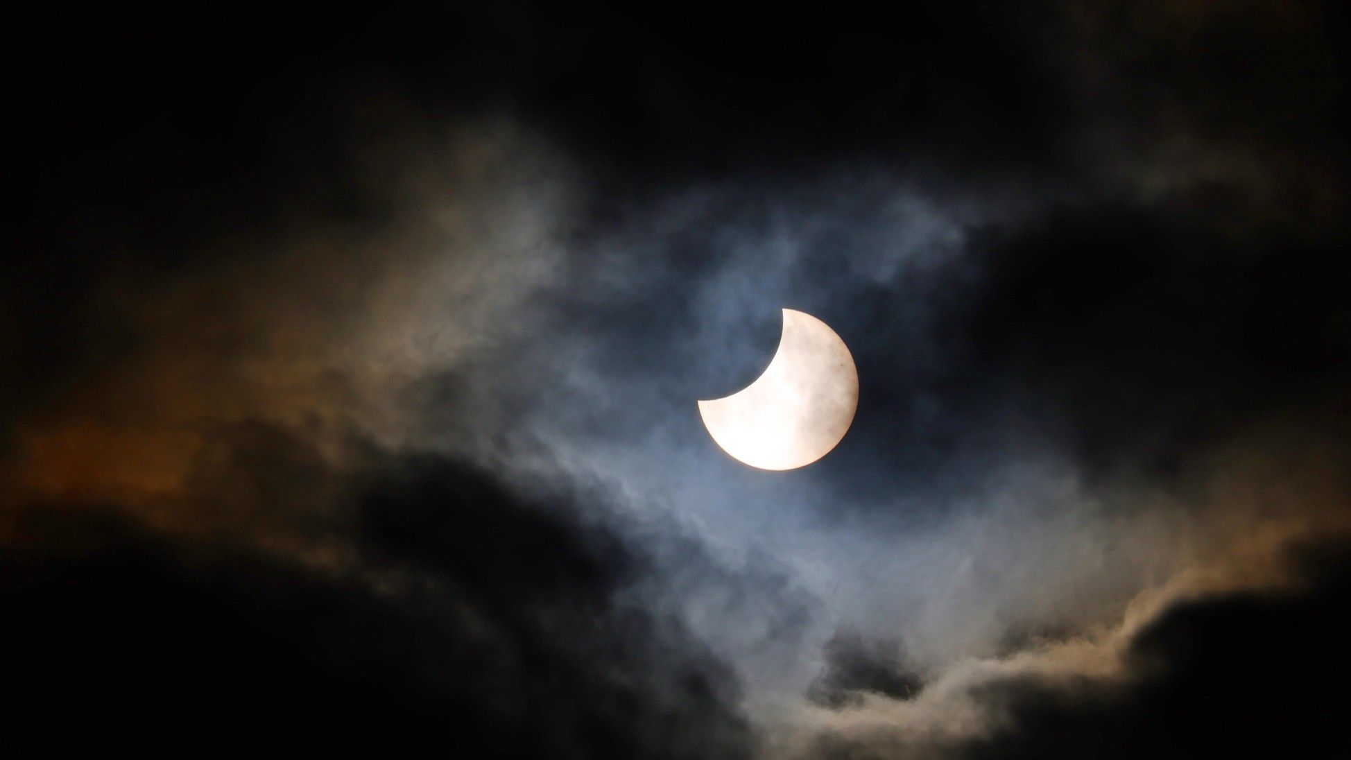 partial solar eclipse appearing from behind some broken cloud