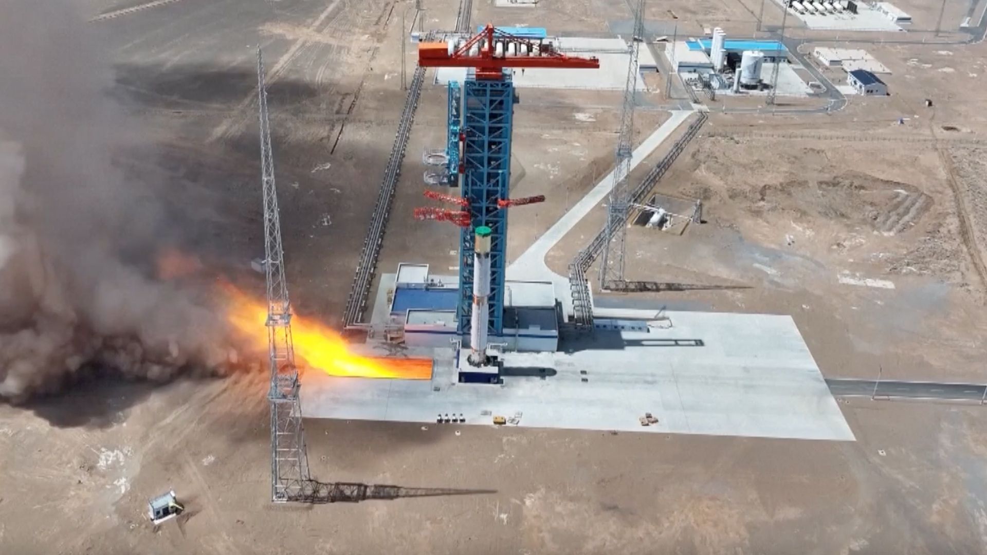 long-distance photo of a white rocket firing its engines on a launch pad